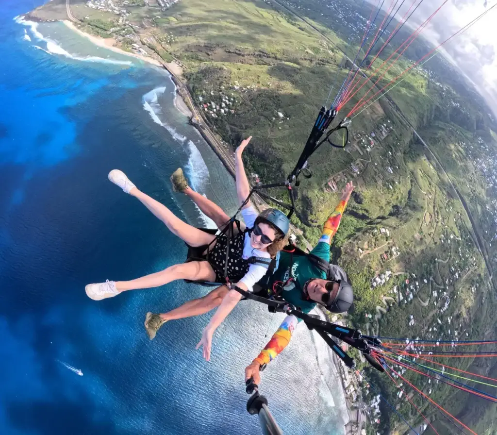 Passagère en baptême de parapente, bras ouverts, survolant le lagon turquoise de Saint-Leu à La Réunion en vol biplace
